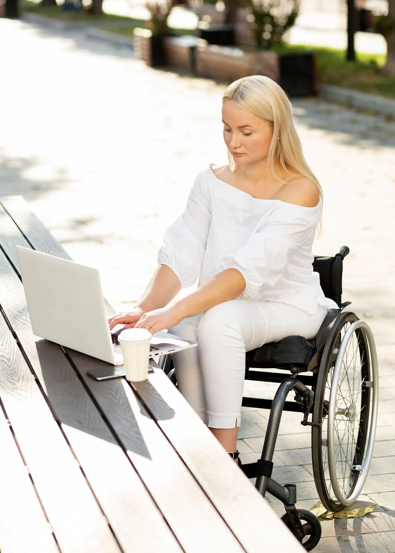 A woman in a wheelchair using a laptop outdoors.